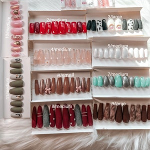 May include: A collection of false nail sets in various styles and sizes, arranged in labeled boxes. Designs include solid colors, glitter, floral, and patterned options. Sizes range from small to large, with medium being the most common.