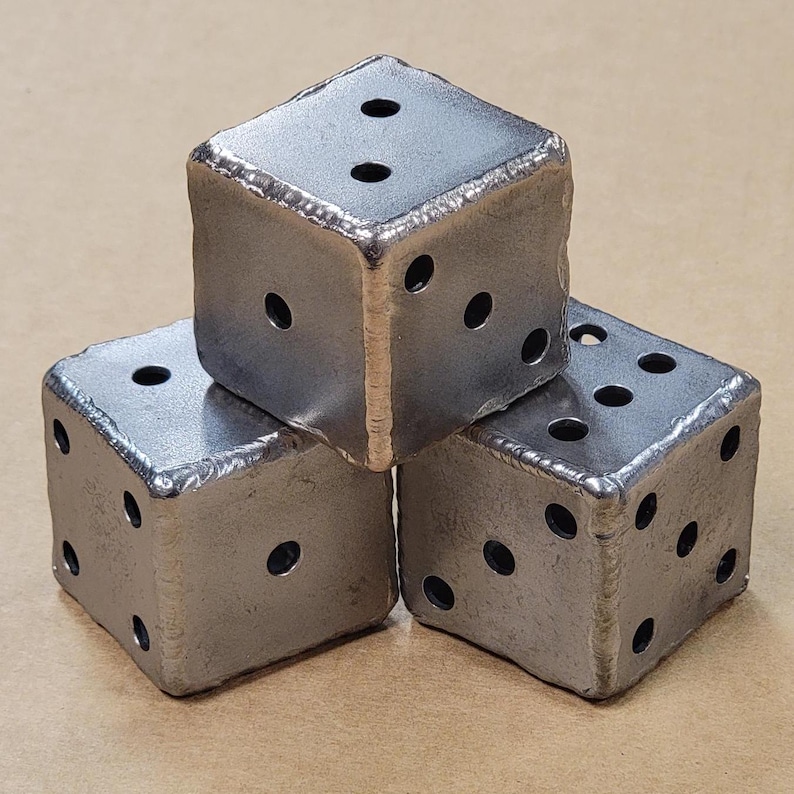 May include: Three metal dice, each with six sides and holes for each number. The dice are made of a dark gray metal and are arranged in a triangular shape.