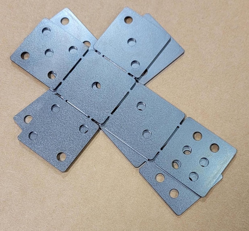 May include: A stack of eight gray metal corner brackets with multiple holes. The brackets are arranged in a cross shape.