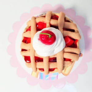 May include: A miniature cherry pie with a lattice crust, filled with red cherry filling and topped with white whipped cream and a red cherry.