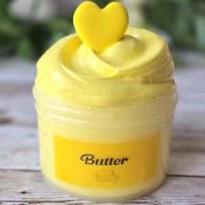 May include: A jar of yellow slime with a yellow heart-shaped decoration on top. The jar has a yellow label with the word "Butter" in a script font and a small hat illustration.