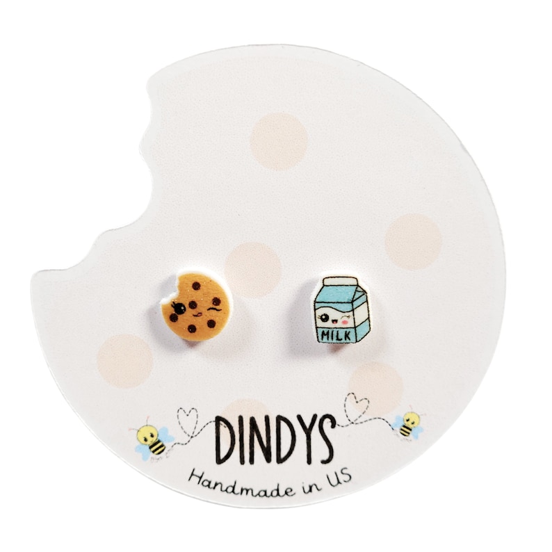 May include: A pair of earrings featuring a cartoon cookie and a cartoon milk carton. The earrings are on a white card with pink polka dots and the text "Dindys Handmade in US".