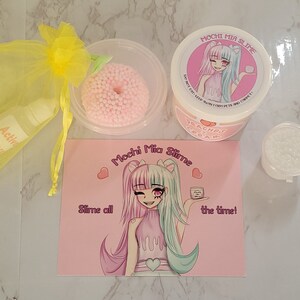 Puede incluir: Un conjunto de productos de slime, que incluye un recipiente de crema de slime con aroma a melocot&oacute;n, un recipiente transparente de slime y un slime rosa con bolitas de espuma. El set incluye una bolsa de organza amarilla con soluci&oacute;n activadora y caramelos. El logotipo "Mochi Mia Slime" est&aacute; presente.