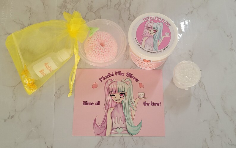 Puede incluir: Un conjunto de productos de slime, que incluye un recipiente de crema de slime con aroma a melocot&oacute;n, un recipiente transparente de slime y un slime rosa con bolitas de espuma. El set incluye una bolsa de organza amarilla con soluci&oacute;n activadora y caramelos. El logotipo "Mochi Mia Slime" est&aacute; presente.