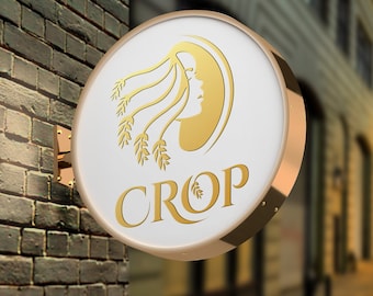 Könnte beinhalten: Ein rundes weißes Schild mit goldfarbenem Rand und goldfarbener Beschriftung. Das Schild trägt die Aufschrift "CROP" und zeigt ein stilisiertes Bild eines Frauenkopfes mit Weizenähren.