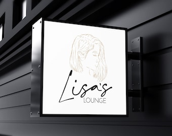 Könnte beinhalten: Ein weißes Schild mit schwarzem Rahmen und einer goldenen Linienzeichnung eines Frauenkopfes. Der Text "Lisa's Lounge" ist in schwarzer Kursivschrift unter der Zeichnung geschrieben.