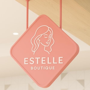 May include: A pink diamond-shaped sign with the name "ESTELLE" and the word "BOUTIQUE" in white lettering. A white line drawing of a woman's face is above the name. The sign is suspended from the ceiling by pink rods.