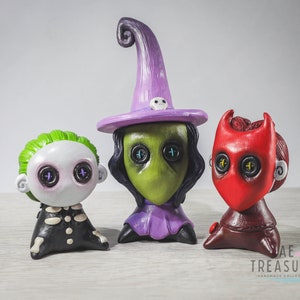 May include: Three handmade Halloween-themed figurines. A green witch with a purple hat and black hair, a green-skinned creature with button eyes, and a red devil with a red mask and button eyes.