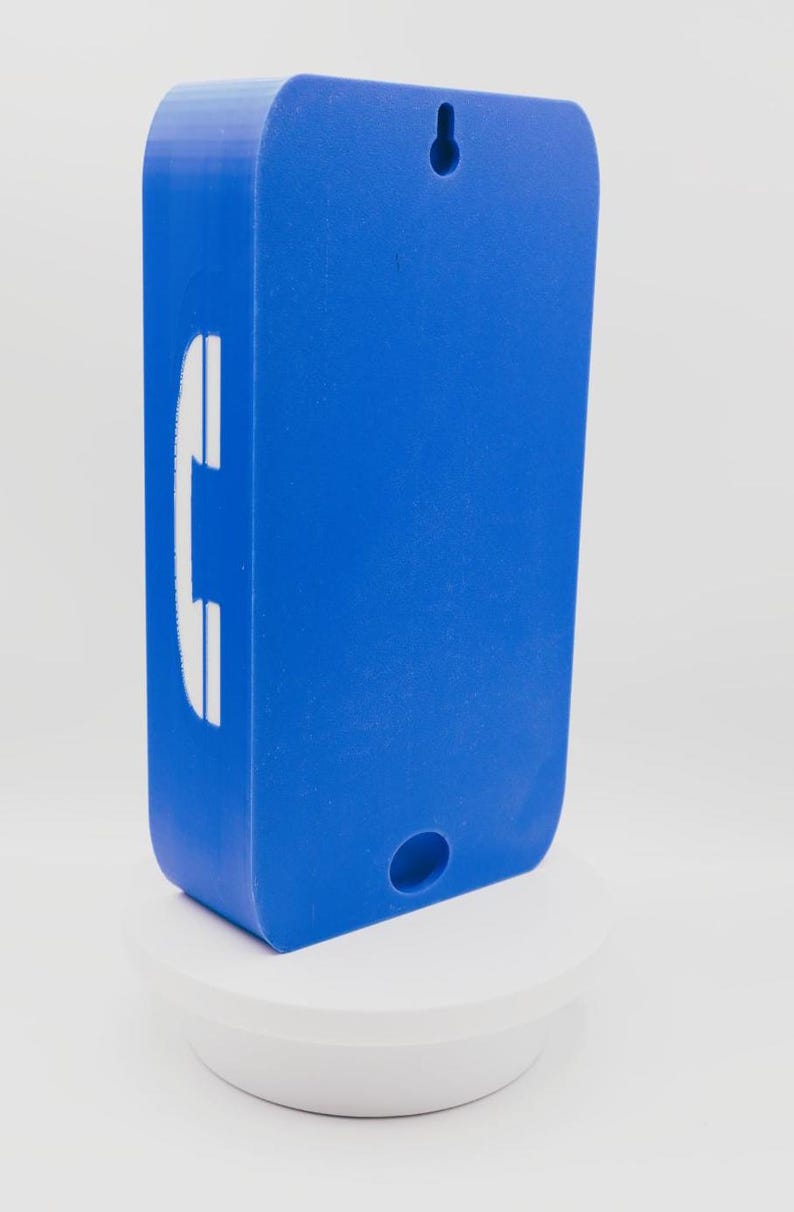May include: A rectangular blue wall-mounted object with rounded corners. The front face features a white telephone handset icon on the left side. There is a keyhole-shaped mounting slot at the top and a circular hole at the bottom center.