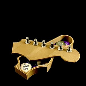 Puede incluir: Una caja de madera con forma de clavijero de guitarra con clavijas plateadas. La caja est&aacute; abierta, revelando p&uacute;as de guitarra con la marca "Tortex". La caja es de madera marr&oacute;n claro sobre un fondo negro.