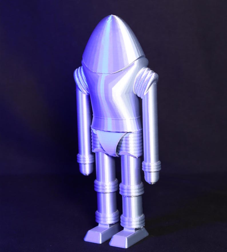 May include: A silver robot toy with a rounded head and segmented limbs. The robot is standing on a black surface.