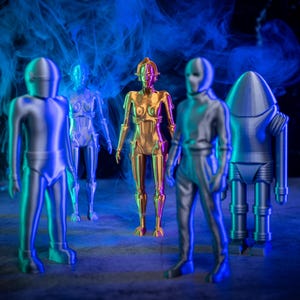 May include: Five metallic robot figurines standing on a gray surface. The robots are silver and gold in color. The background is dark with blue and purple smoke.