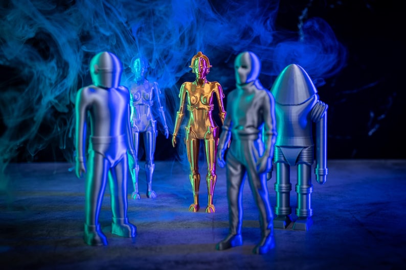 May include: Five metallic robot figurines standing on a gray surface. The robots are silver and gold in color. The background is dark with blue and purple smoke.