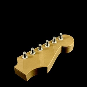 Puede incluir: Un clavijero de guitarra marr&oacute;n claro con clavijas plateadas. El clavijero tiene una forma cl&aacute;sica con seis clavijas. La veta de la madera es visible en la superficie. El fondo es negro.
