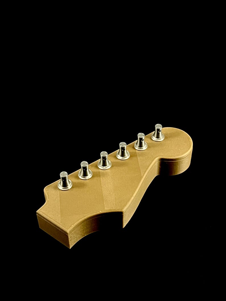 Puede incluir: Un clavijero de guitarra marr&oacute;n claro con clavijas plateadas. El clavijero tiene una forma cl&aacute;sica con seis clavijas. La veta de la madera es visible en la superficie. El fondo es negro.