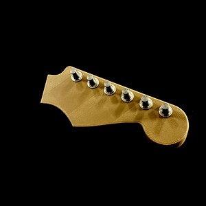 Puede incluir: Primer plano de un clavijero de guitarra de madera clara, con seis clavijas plateadas. La madera tiene un aspecto liso y sin terminar. El fondo negro s&oacute;lido resalta la pieza de la guitarra.