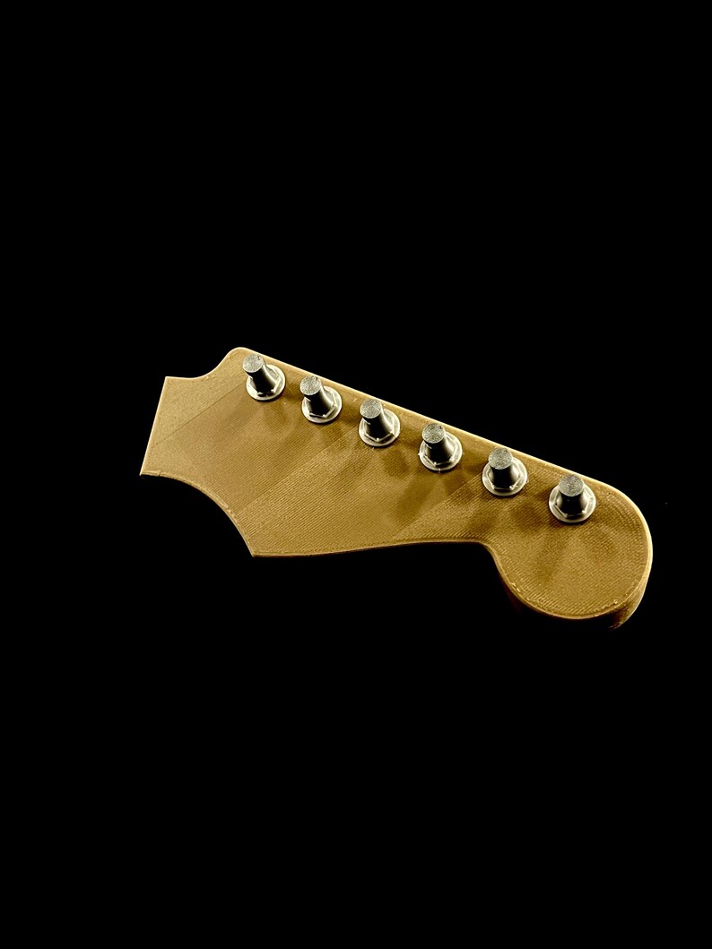 Puede incluir: Primer plano de un clavijero de guitarra de madera clara, con seis clavijas plateadas. La madera tiene un aspecto liso y sin terminar. El fondo negro s&oacute;lido resalta la pieza de la guitarra.