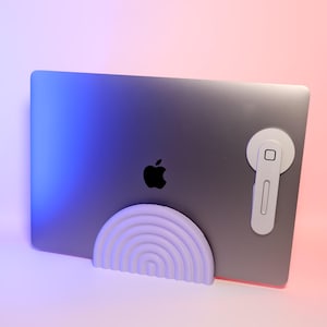 May include: A white laptop stand with a rainbow design. The stand is made of a smooth, hard plastic and is designed to elevate a laptop for better ergonomics. The stand is shown with a laptop resting on it.
