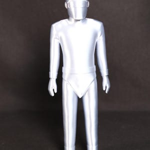 May include: A silver-colored, 3D printed figurine of a person wearing a helmet and a full-body suit.
