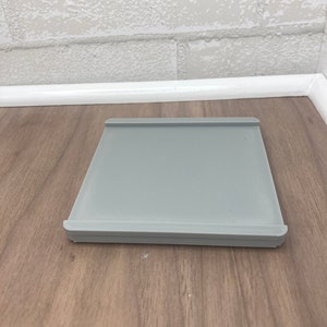 Könnte beinhalten: Eine graue quadratische Backmatte aus Silikon mit erhöhten Rändern. Die Matte liegt auf einer Holzoberfläche.