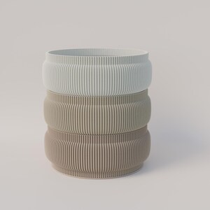 May include: Three stacked, cylindrical planters in light blue, beige, and tan. Each planter features a ribbed texture, forming a vertical striped pattern. The planters have a rounded, bulbous shape.