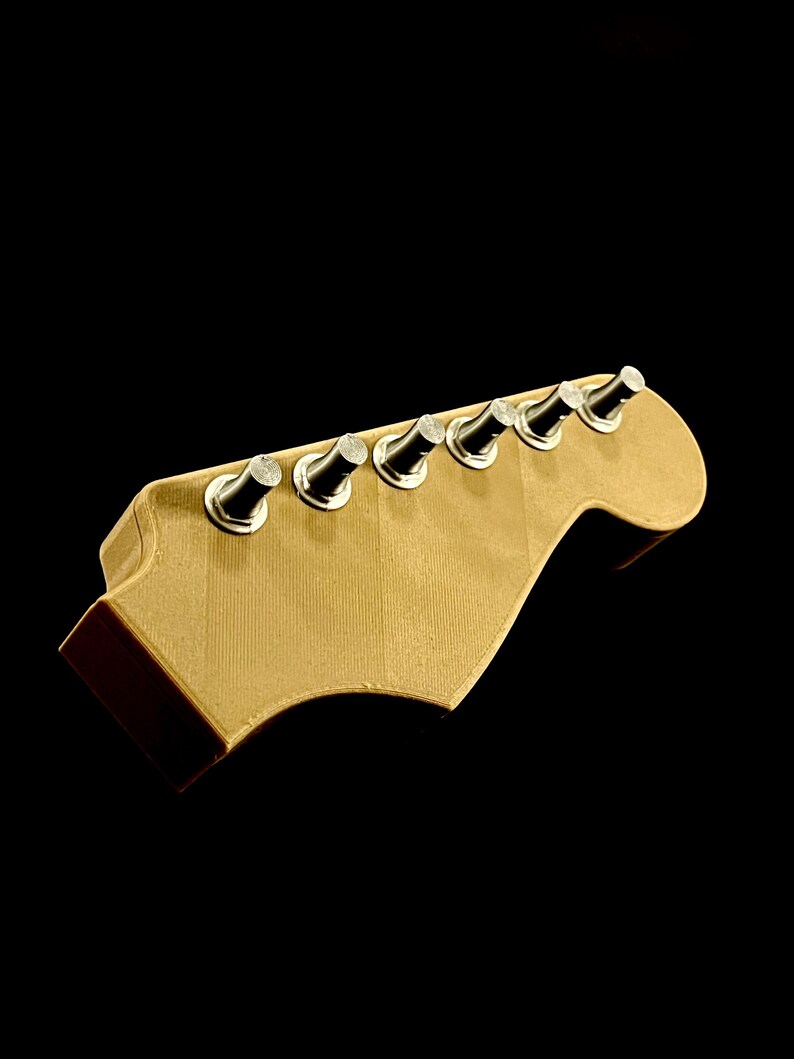 Puede incluir: Un clavijero de guitarra con seis clavijas. El clavijero es de color beige claro, con un borde marr&oacute;n oscuro. Las clavijas son plateadas y negras. El fondo es negro.