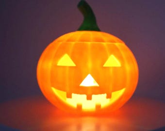 May include: A glowing orange jack-o'-lantern with a green stem. The pumpkin features two triangular eyes, a triangular nose, and a jagged mouth with square teeth, all illuminated from within to create a bright, warm light against a dark background.