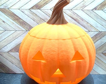 May include: A large orange plastic jack-o'-lantern with a carved face and a brown stem. The pumpkin is lit from inside, creating a warm glow.