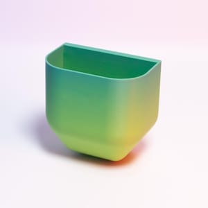 Könnte beinhalten: Ein runder Wand-Pflanztopf mit einem Farbverlauf von Grün zu Gelb.