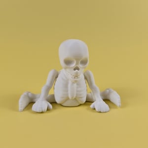May include: White plastic skeleton figurine with a skull head and articulated limbs. The skeleton is sitting with its legs crossed and its arms resting on its knees.