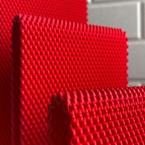 May include: Close-up of three red textured rectangular mats with a repeating pattern of small, raised bumps. The mats are stacked, revealing a textured edge. The background is a light grey, brick-like wall.