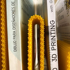 May include: A close-up of books and a yellow, concertina-style divider. The books have white spines with text in Spanish and English. The divider is a bright yellow colour and has a zig-zag edge.
