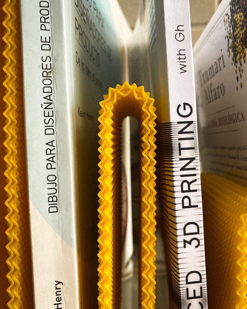 May include: A close-up of books and a yellow, concertina-style divider. The books have white spines with text in Spanish and English. The divider is a bright yellow colour and has a zig-zag edge.