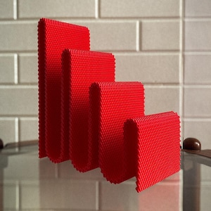 May include: Four bright red, textured, rectangular objects of varying heights are arranged in a row. The objects have a ridged edge and are set against a light grey brick wall. The objects appear to be decorative.