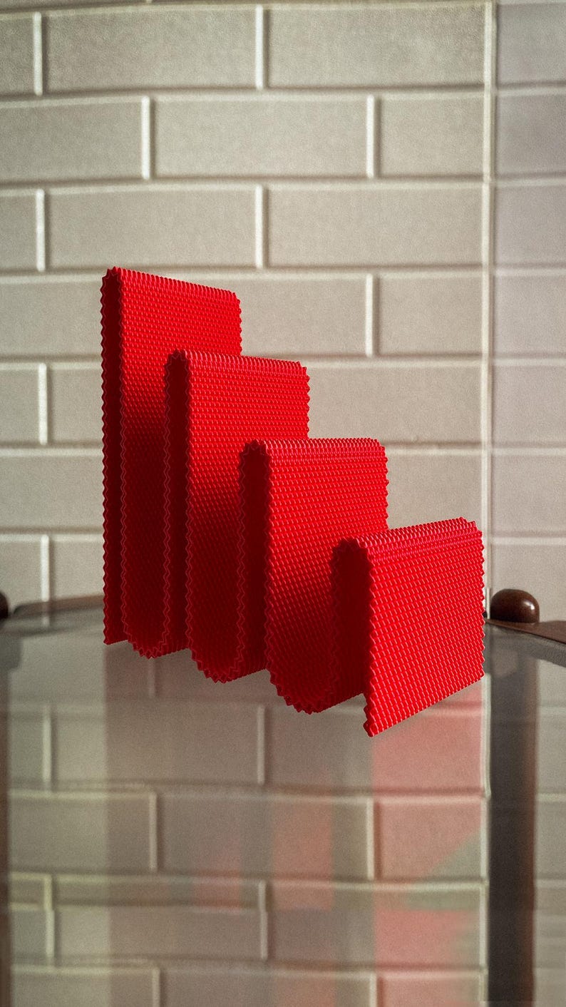 May include: Four bright red, textured, rectangular objects of varying heights are arranged in a row. The objects have a ridged edge and are set against a light grey brick wall. The objects appear to be decorative.