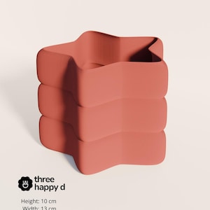 May include: A coral-colored, star-shaped container with a wavy design. The container is 10 cm high and 13 cm wide. The text "three happy d" is printed on the side.