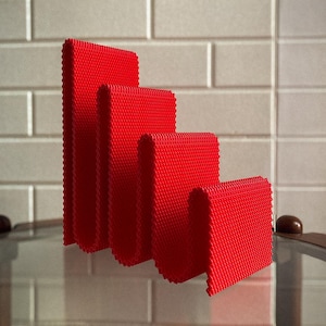 May include: Four red, textured, rectangular objects of varying heights are arranged in a stepped pattern. The objects have a woven appearance and are set against a neutral, tiled background. The objects are reflected on a glass surface.