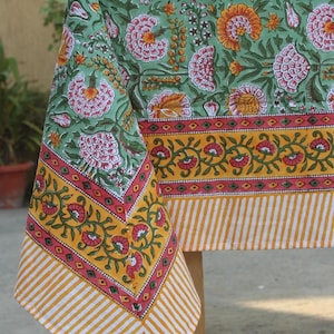 May include: A green tablecloth with a floral print and yellow and pink border. The tablecloth has a striped pattern on the bottom edge.
