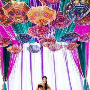 Puede incluir: Una ceremonia de boda decorada con coloridas sombrillas estampadas que cuelgan de un techo de tela morada, rosa y turquesa.