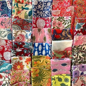 Puede incluir: Una colección de cuadrados de tela doblados en varios colores y estampados florales. Las telas incluyen tonos de rojo, azul, rosa y amarillo, con diseños de flores, hojas y otros motivos naturales. Los textiles están cuidadosamente apilados.
