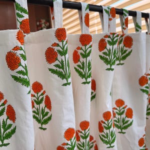 May include: White cotton curtains with a repeating pattern of orange floral designs and green leaves. The curtains are hanging from a black rod. The floral pattern is a bold, eye-catching design.