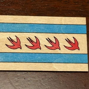 May include: A wooden plaque with the Chicago flag design. The flag features four red stylized birds flying in a row against a white background with three blue horizontal stripes.