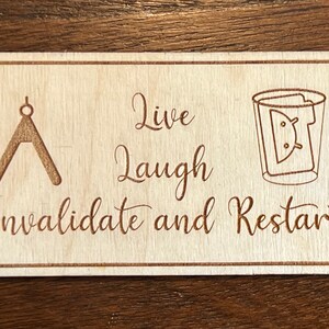 Peut inclure: Une pancarte en bois avec le texte "Live Laugh Invalidate and Restart" et une boussole et un verre avec un robot Android à l'intérieur.