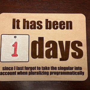 May include: A wooden sign with the text "It has been 1 days since I last forgot to take the singular into account when pluralizing programmatically."