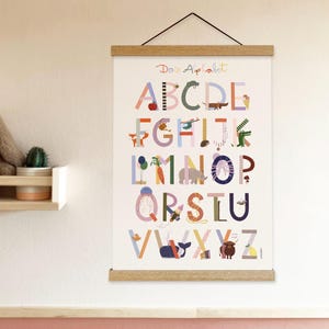 May include: A colorful alphabet poster with the text "Dans Alphabet" at the top. Each letter is illustrated with a corresponding image, such as an apple for A and a whale for V. The poster is held by wooden bars and a black string.
