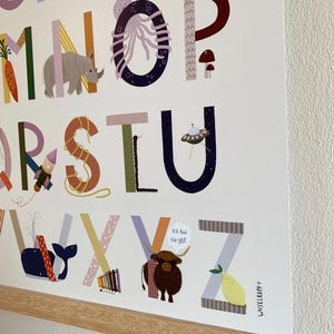 May include: A colorful alphabet poster with each letter illustrated with a corresponding image. The poster features a whale, a rhino, and a yak with the text "Ich Bin Ein Yak". The poster is framed with a light wood frame.