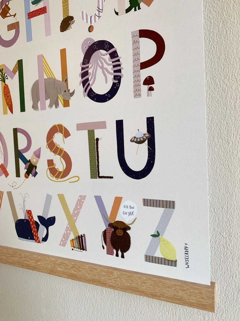 May include: A colorful alphabet poster with each letter illustrated with a corresponding image. The poster features a whale, a rhino, and a yak with the text "Ich Bin Ein Yak". The poster is framed with a light wood frame.