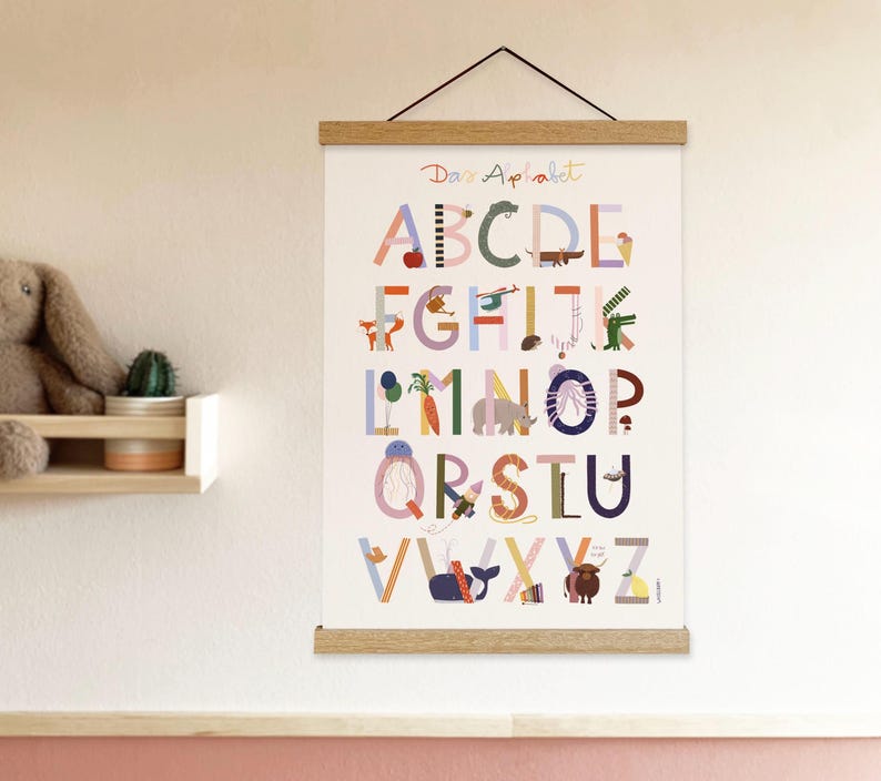 May include: A colorful alphabet poster with the text "Dans Alphabet" at the top. Each letter is illustrated with a corresponding image, such as an apple for A and a whale for V. The poster is held by wooden bars and a black string.