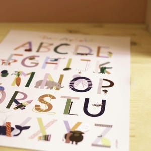 May include: A colorful alphabet poster with each letter illustrated with a corresponding image. The letters are in various colors, and the illustrations include a carrot, an elephant, and a whale. The poster is on a light-colored surface.