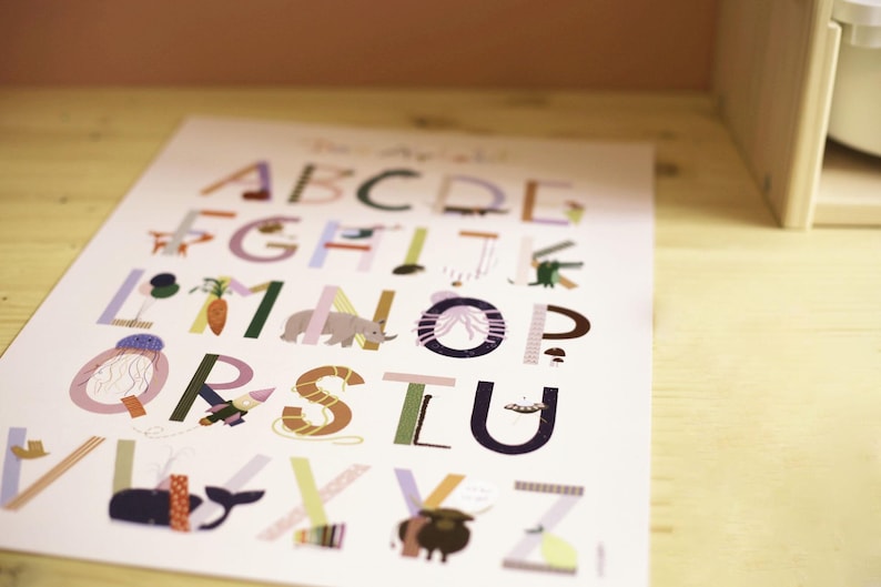 May include: A colorful alphabet poster with each letter illustrated with a corresponding image. The letters are in various colors, and the illustrations include a carrot, an elephant, and a whale. The poster is on a light-colored surface.